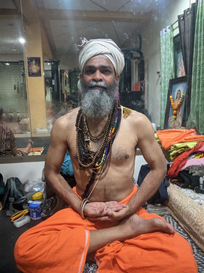Guru Sanjay Nath in white turban and saffron dhoti, seated at the mandir