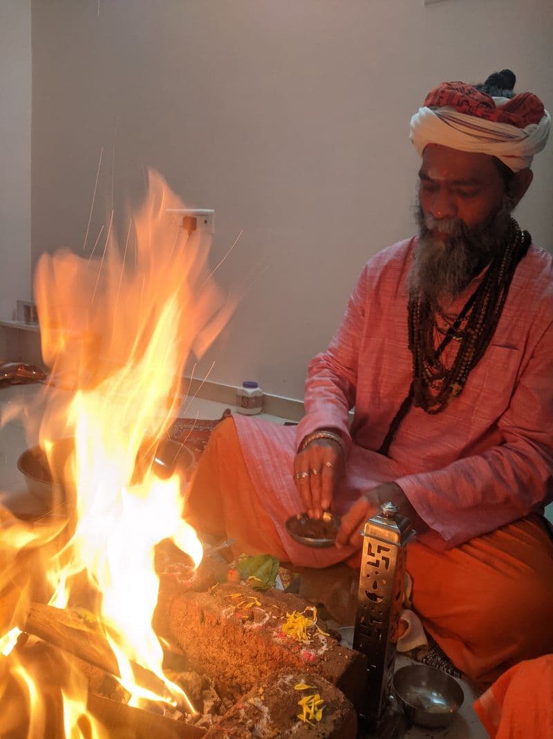 The Guru seated beside the havan kund, flames filling the frame