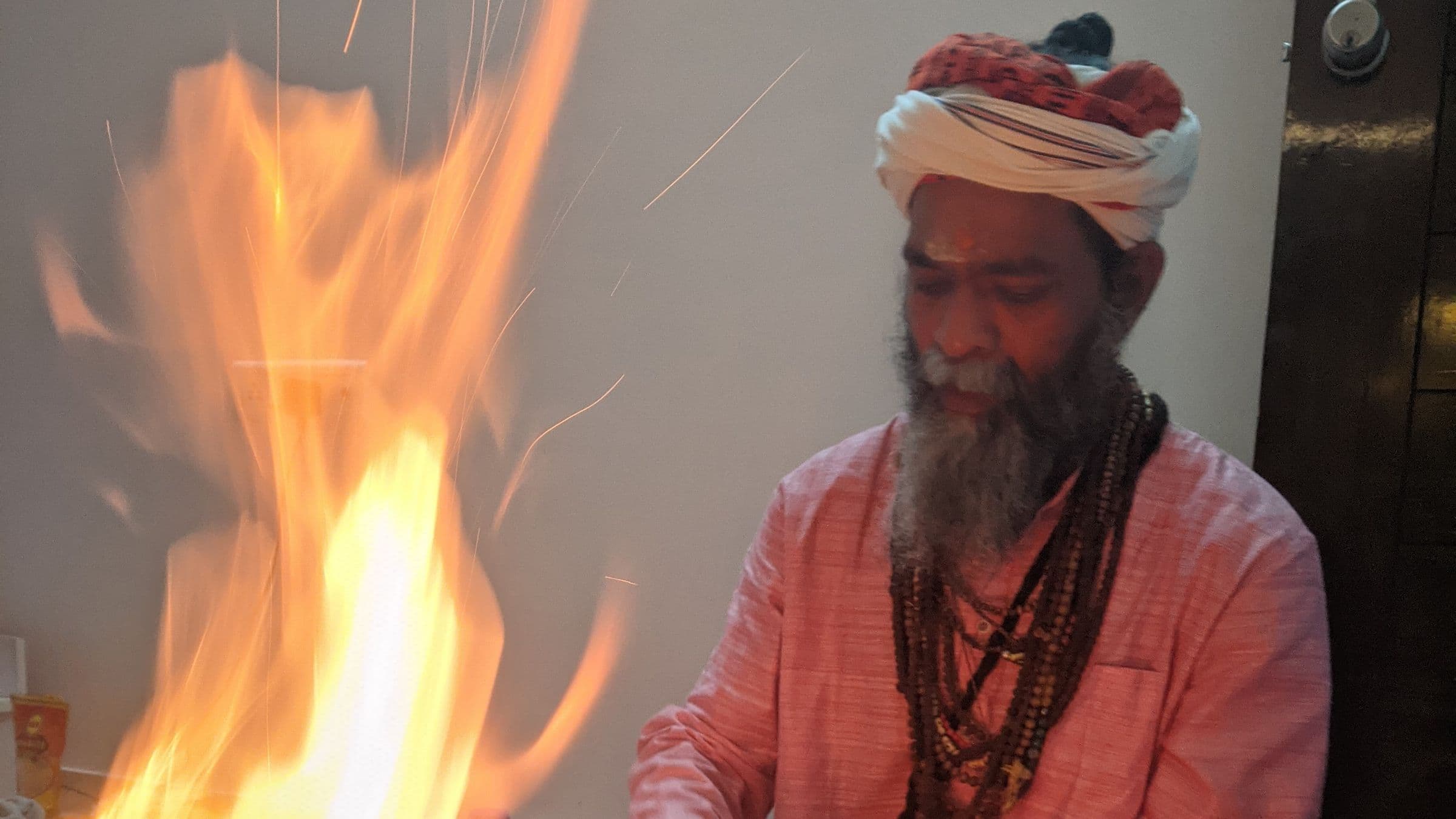 Guru Sanjay Nath at the havan fire, flames rising beside him and sparks in the air